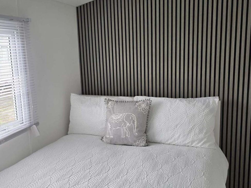 A bed with a decorative pillow against a striped wall at Luxury Cosy Caravan in Cresswell Northumberland