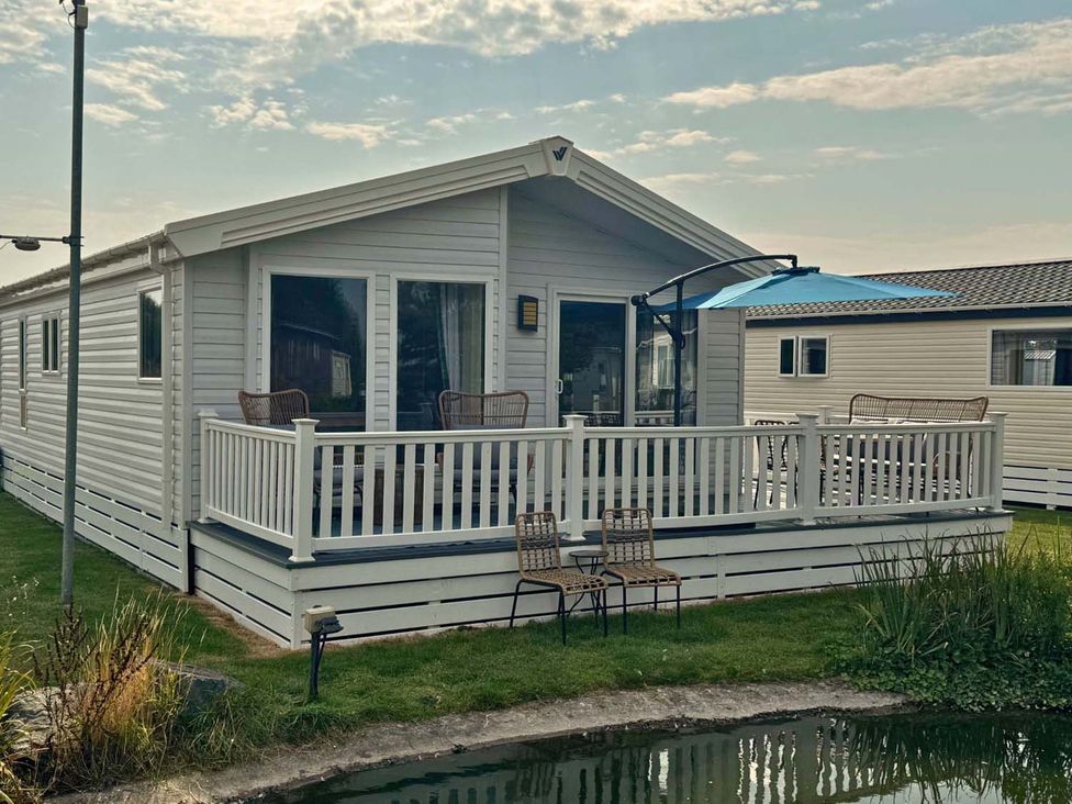 A mobile home with a deck and chairs at a property near a pond