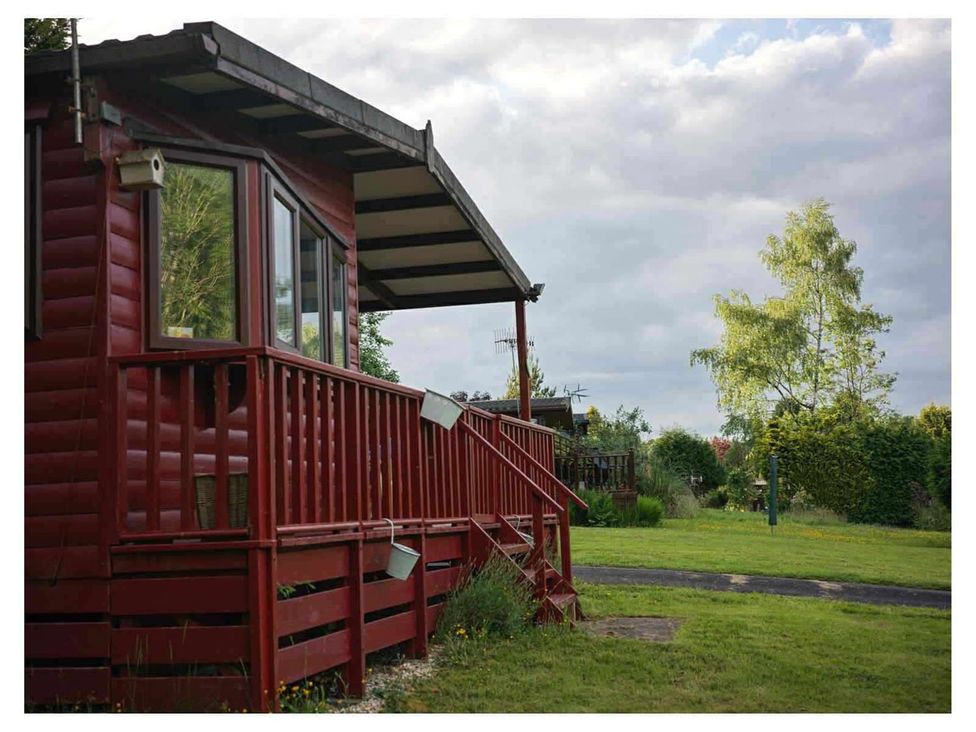 A red cabin with a deck and garden space at The Old Barn in Builth Wells