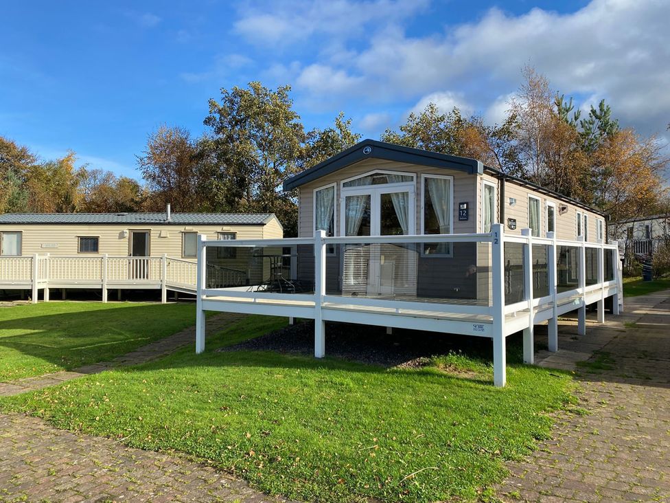 A caravan with a deck and grassy area at the holiday park