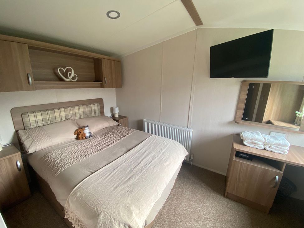 A bedroom with a bed, television, and dressing table at the property location