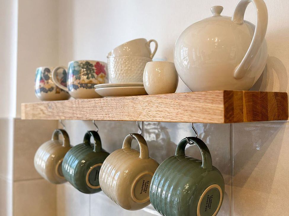 A kitchen shelf with teapot, mugs, cups, and a plate