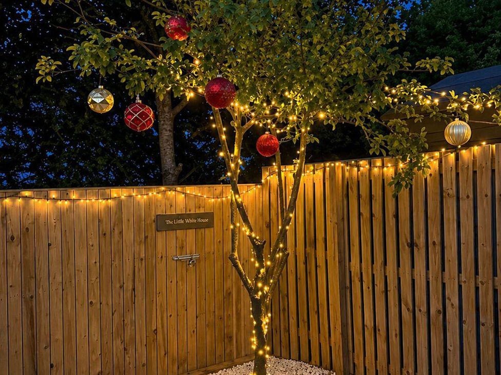 A tree with lights and ornaments near a wooden fence at The Little White House in an outdoor setting