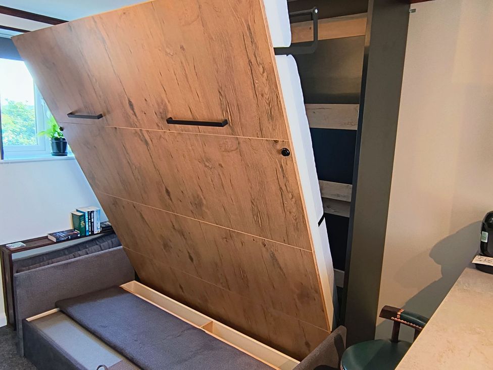 A murphy bed in the upright position with a bookshelf in the living room at Studio Sleeps 2 with Parking and Garden Trewidland near Liskeard