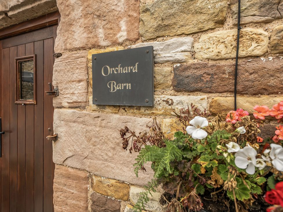 A sign labeled Orchard Barn at the entrance with flowers at Orchard Barn Waterhouses