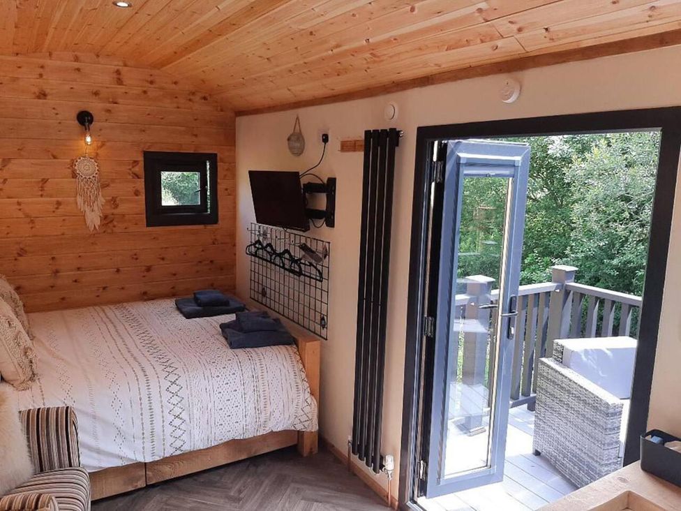 A bedroom with a bed and a door leading to a deck at Min yr Afon Cabin Sleeps2 Hot Tub Parking Gwalchmai