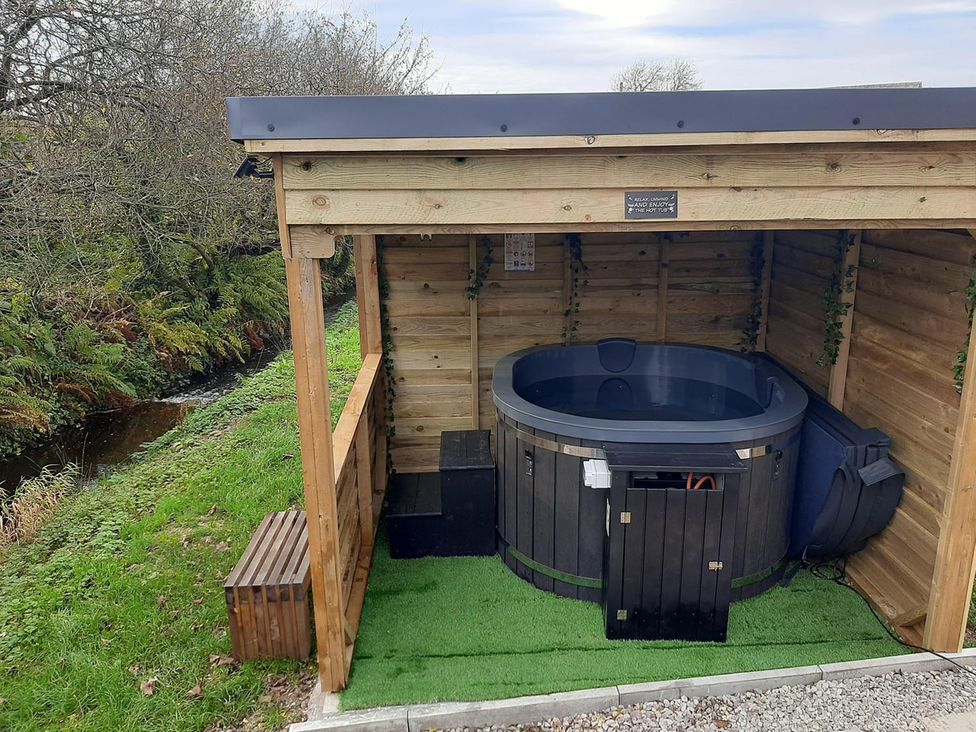 An outdoor hot tub in a wooden shelter at Min yr Afon Cabin Sleeps2 Hot Tub Parking Gwalchmai