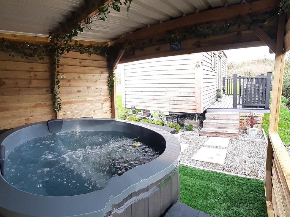 An outdoor hot tub adjacent to a wooden cabin at Min yr Afon Cabin Sleeps2 Hot Tub Parking in Gwalchmai