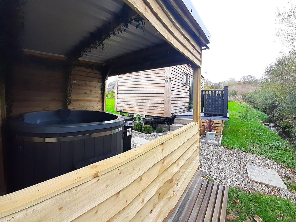 An outdoor area with a hot tub and wooden cabin at Min yr Afon Cabin Sleeps2 Hot Tub Parking in Gwalchmai