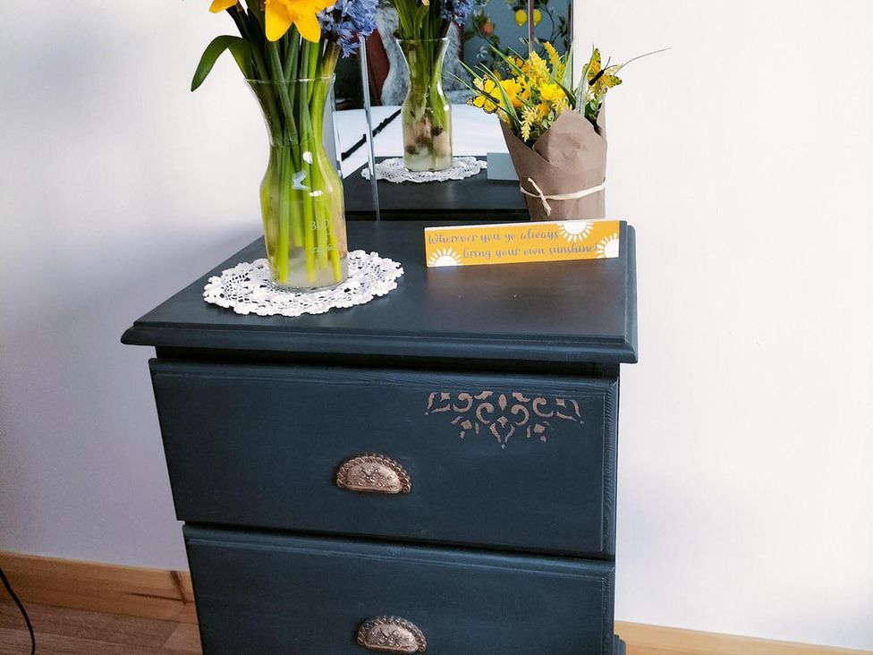 A bedside table with flowers and a decorative sign in a bedroom