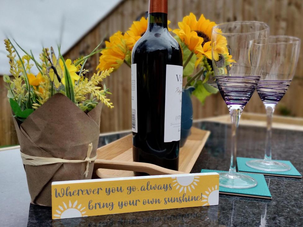 A wine bottle, glasses, flowers, and a decorative sign on a tray outdoors