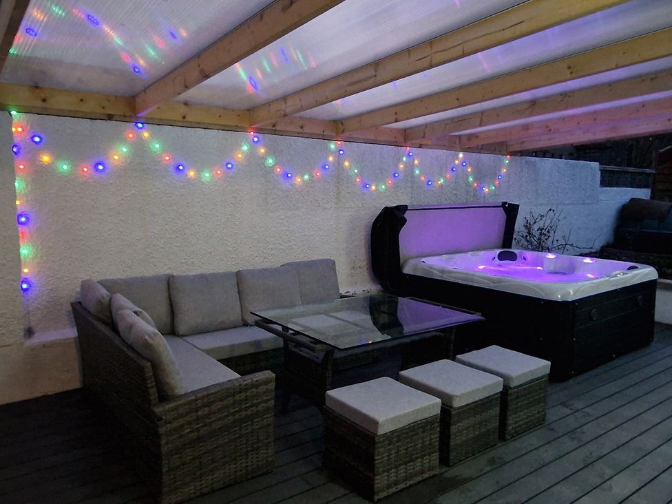 An outdoor seating area with a glass table and hot tub at The Old Barn in Manchester