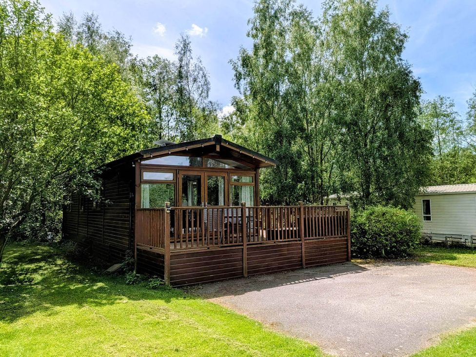 A cabin with a deck surrounded by trees at Felmoor Park Northumberland Lodge with Hot Tub Felmoor Park near Felton