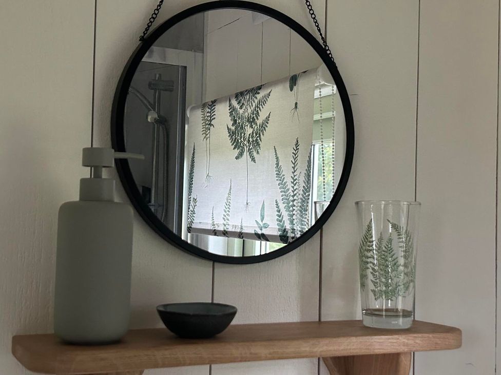 A mirror with a soap dispenser and a glass on a wooden shelf in a bathroom