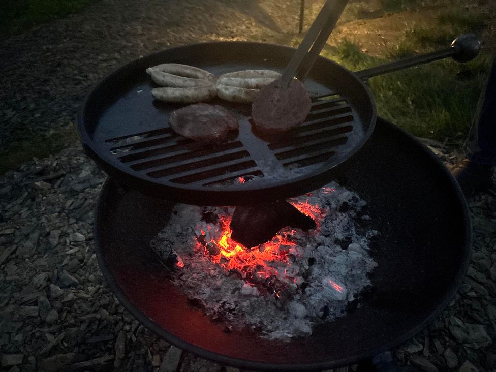 A grill with sausages and hamburger cooking over charcoal