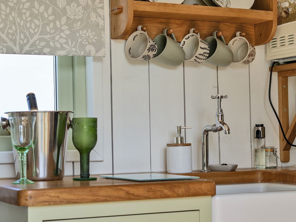 A kitchen with mugs on a shelf and glassware on the countertop at Cosy Luxury Owls Roost Hut with Private Hot Tub near Little Deptford Farm