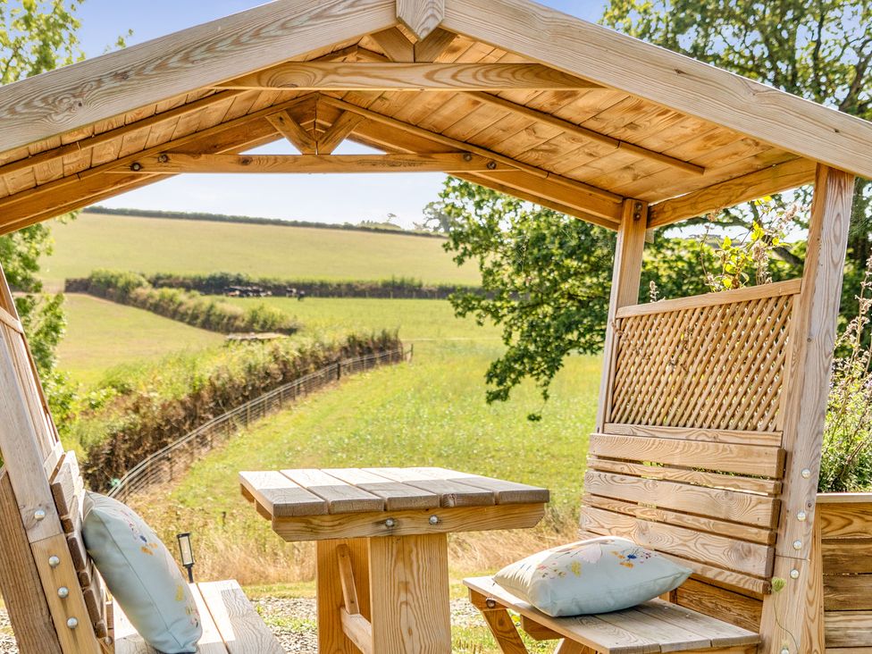 A wooden gazebo with a table and benches at Cosy Luxury Owls Roost Hut with Private Hot Tub near Little Deptford Farm near Umberleigh
