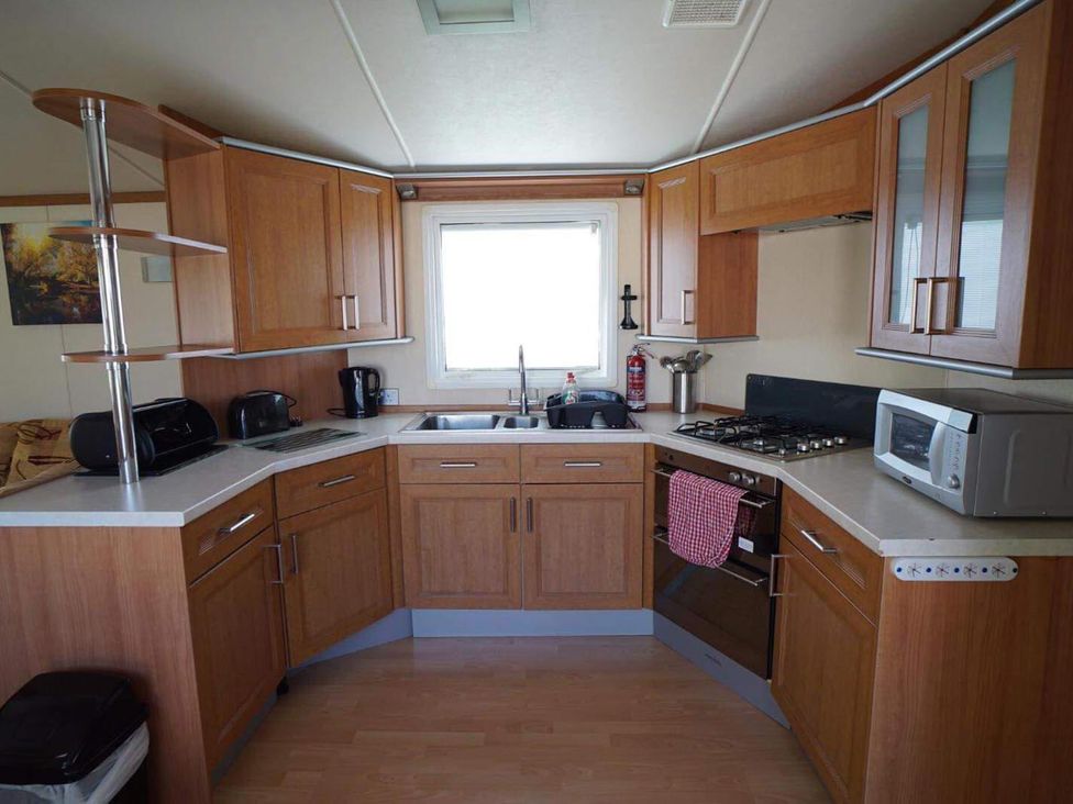 A kitchen with cabinets, sink, gas stove and microwave at Cozy 2 bedroom Coastal Chalet in Heacham
