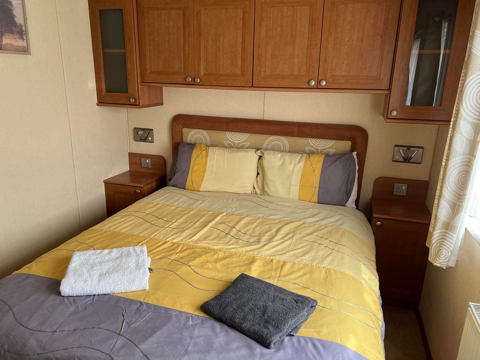 A bedroom with a bed, bedside tables, and shelves at Cozy 2 bedroom Coastal Chalet in Heacham