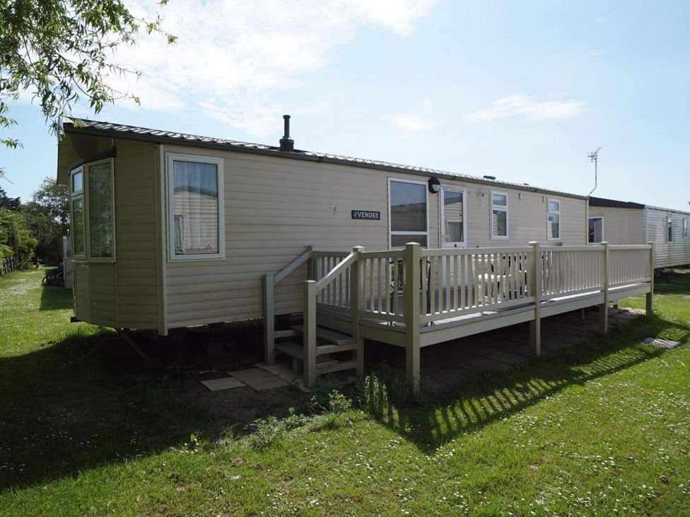A mobile home with a deck and steps in a grassy area at Cozy 2 bedroom Coastal Chalet in Heacham