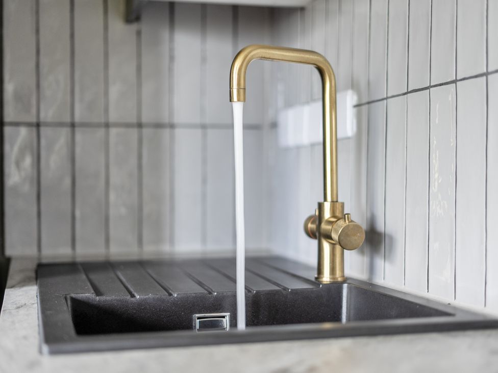 A sink with a gold faucet dispensing water at a kitchen