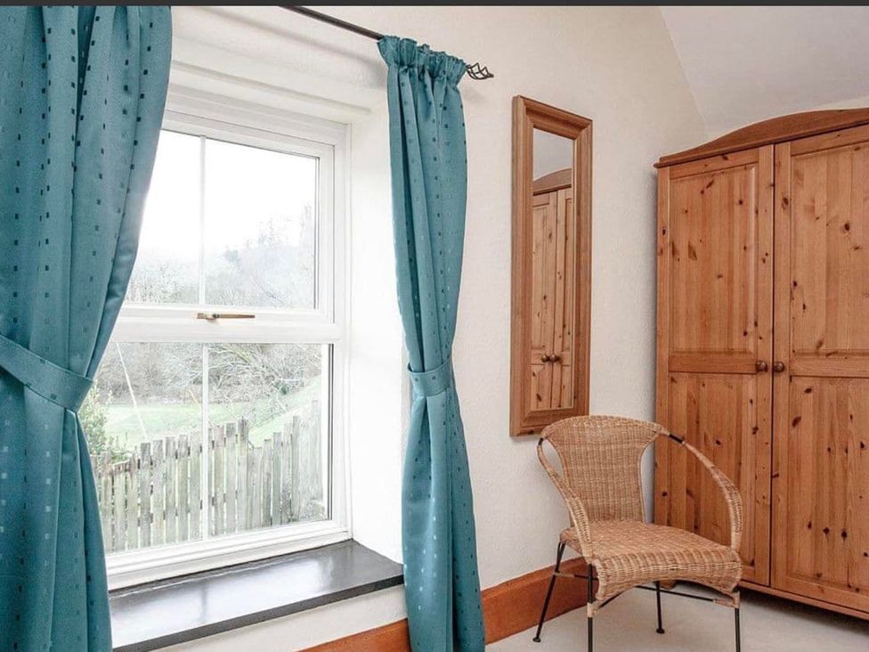 A bedroom with a window, curtains, a chair, wardrobe and mirror at 