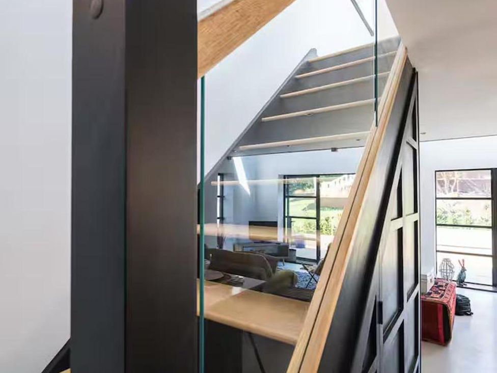 A staircase with a glass railing and wooden handrail leading to a living room area at a modern property