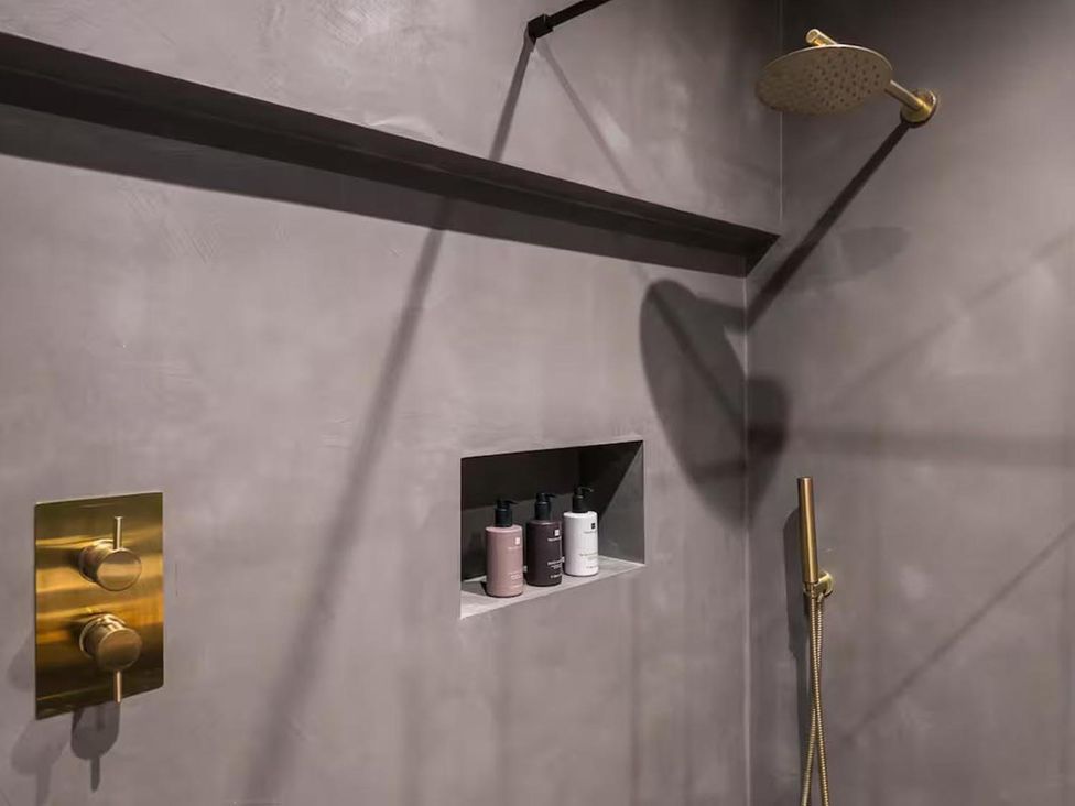 A shower with a gold shower head and control panel in a bathroom