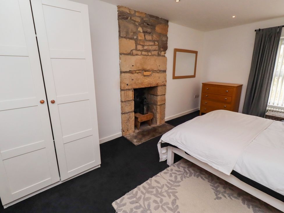 A bedroom with a fireplace and wardrobe at Cooper's Cottage in Morpeth