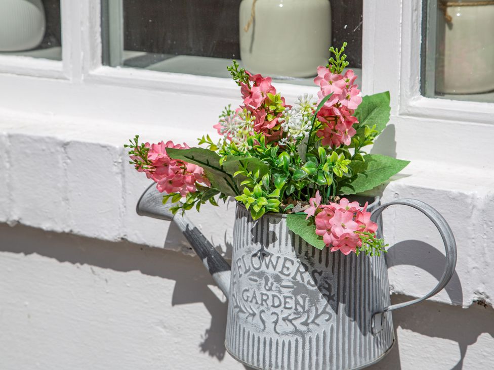 A watering can with artificial flowers on a window ledge at Hudson House
