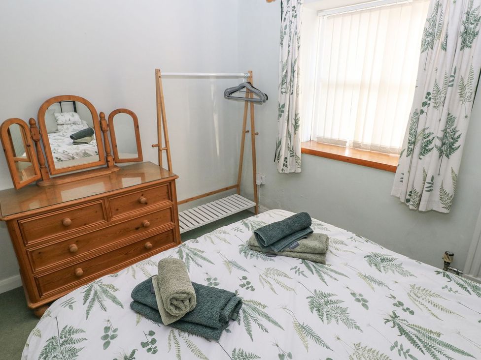 A bedroom with a bed, dresser, and clothes rack at Barn Cottage in Haverfordwest