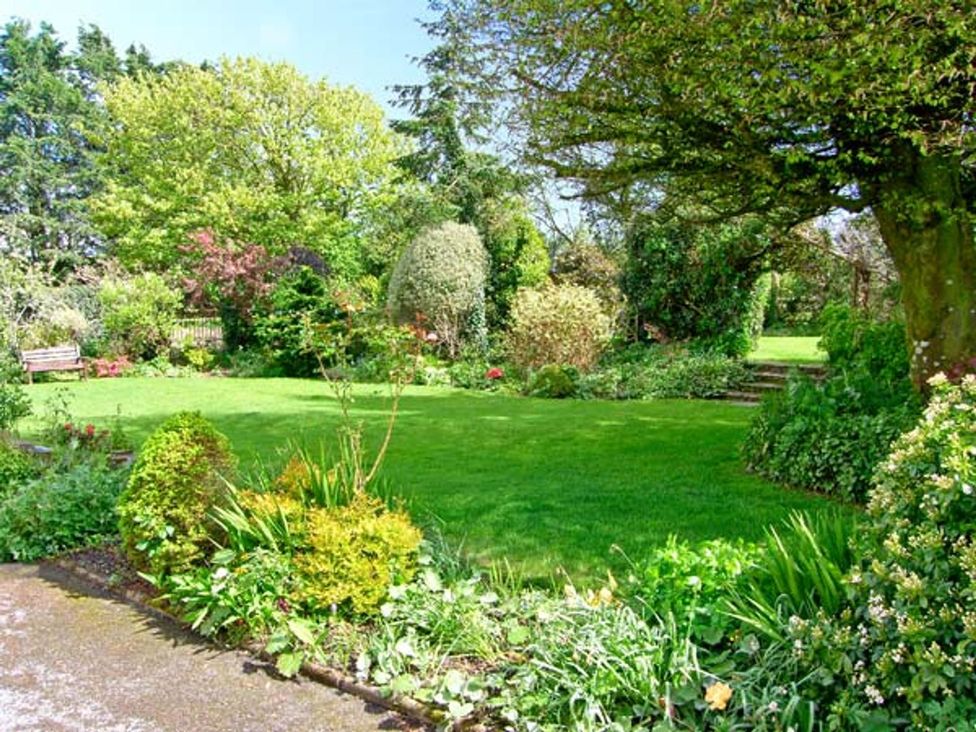 A garden with grass, trees, and flower beds at Barn Cottage in Haverfordwest
