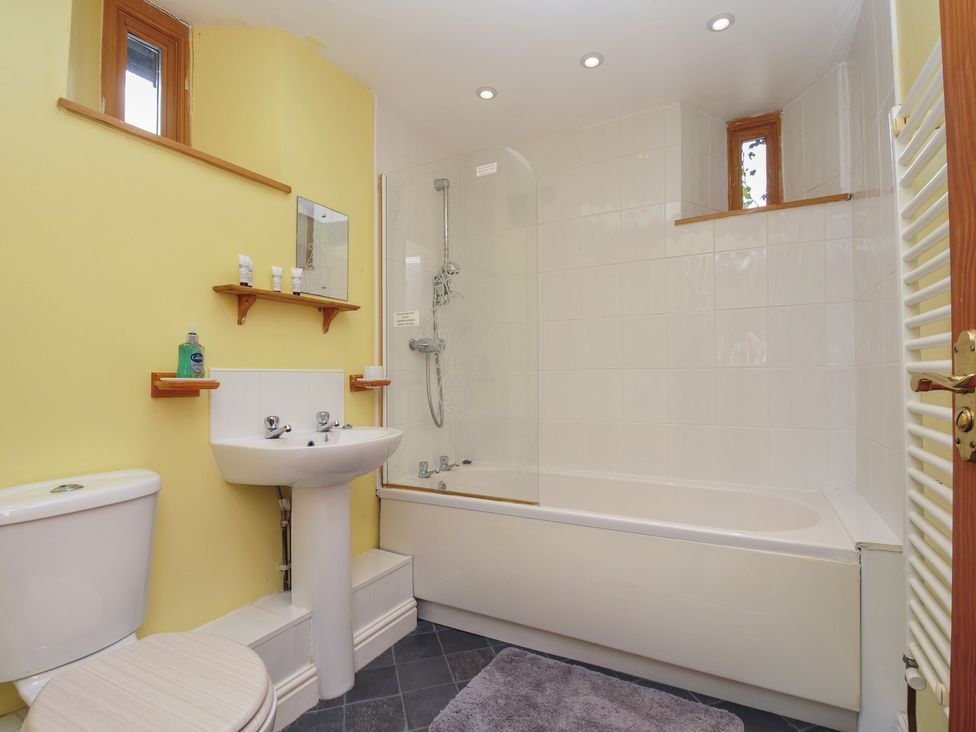A bathroom with a bathtub, toilet, sink and shelves at The Old Wagon House in Torpoint
