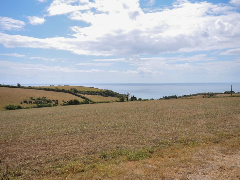 A grassy field with a view of the sea and hills at The Old Wagon House in Torpoint