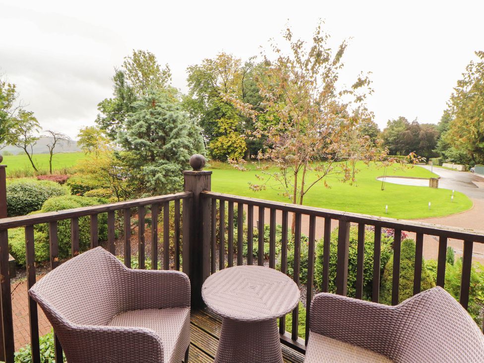 A balcony with chairs and table overlooking a green area at Ullswater Apartment- No 15