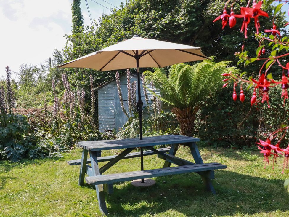 A picnic table with an umbrella and greenery at The Jingle House in Tregony
