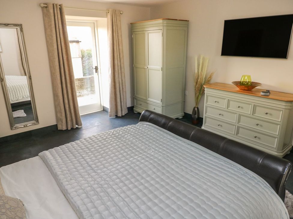A bedroom with a bed, mirror, wardrobe, television, and dresser at The Cartbarn at Cadwgan Farm near Whitland