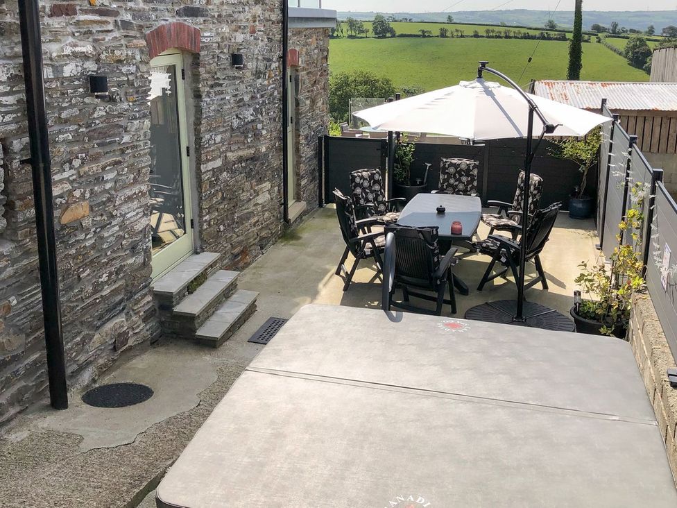 An outdoor patio with a hot tub, table, and chairs at The Cartbarn at Cadwgan Farm near Whitland