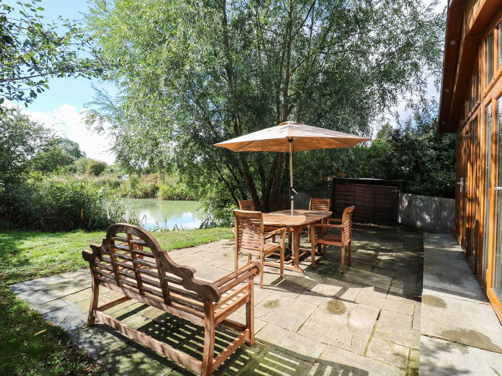 A garden with a table and chairs beside a pond at Oak Lodge Battisford near Stowmarket