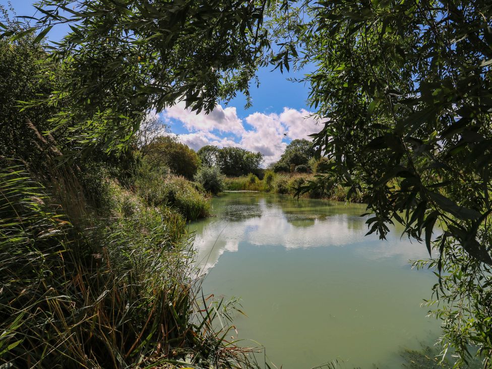 A tranquil scene by the water with trees and clouds at Oak Lodge Battisford near Stowmarket