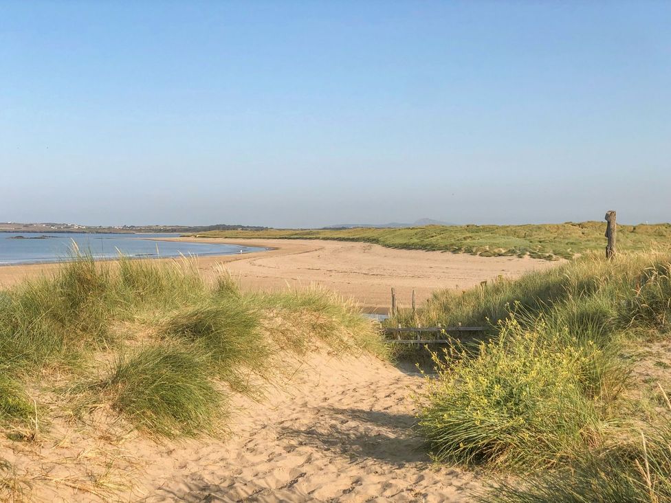 A view of a sandy beach with grass and water at Bryn Tirion - Rhosneigr