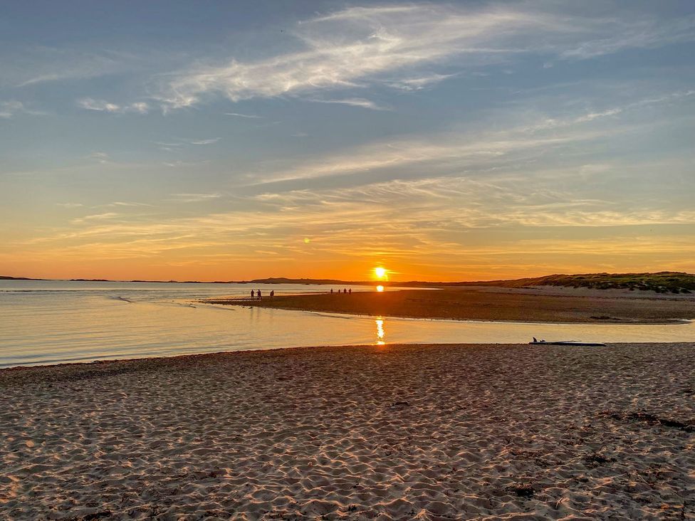 A sunset over water with people walking on the sand at Bryn Tirion - Rhosneigr