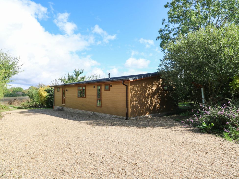 A wooden lodge with gravel driveway and trees at Cherry Lodge Battisford near Stowmarket