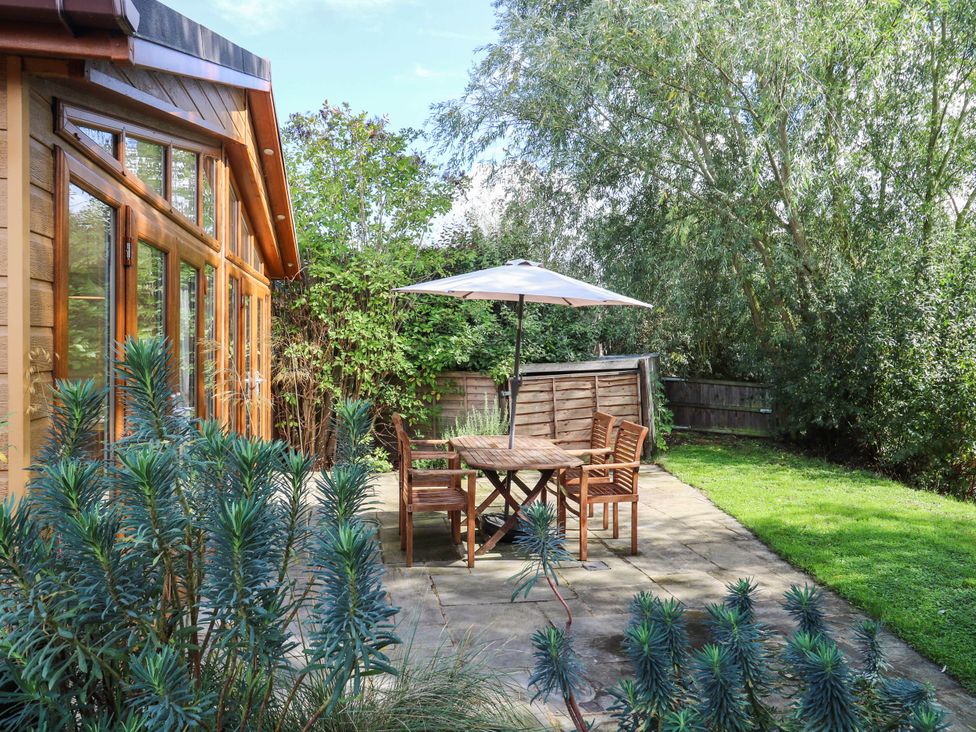 A garden with a table and chairs under an umbrella at Willow Lodge in Stowmarket