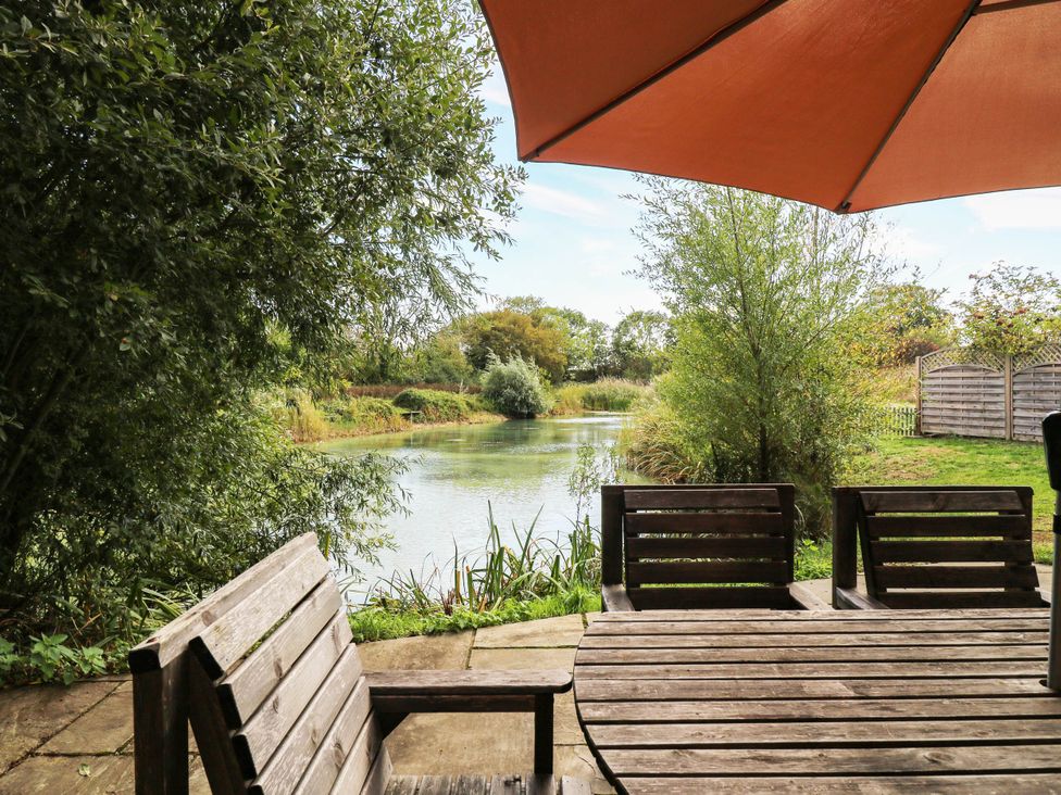 A garden view with a table and chairs overlooking a body of water at Willow Lodge Stowmarket