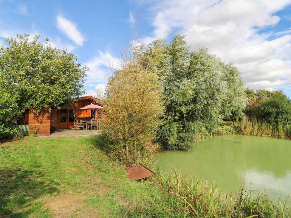 A lodge and pond surrounded by grass and trees at Willow Lodge Stowmarket