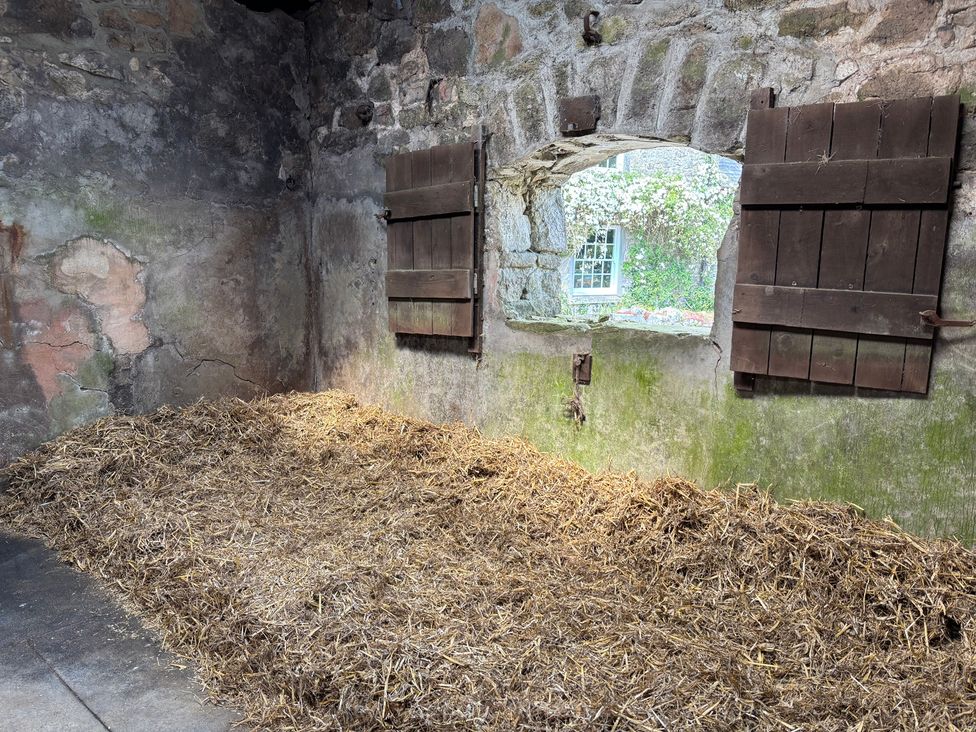 A barn interior with straw on the floor and a window with wooden shutters at Brimble Cottage at Dockwell Farm near Widecombe-In-The-Moor