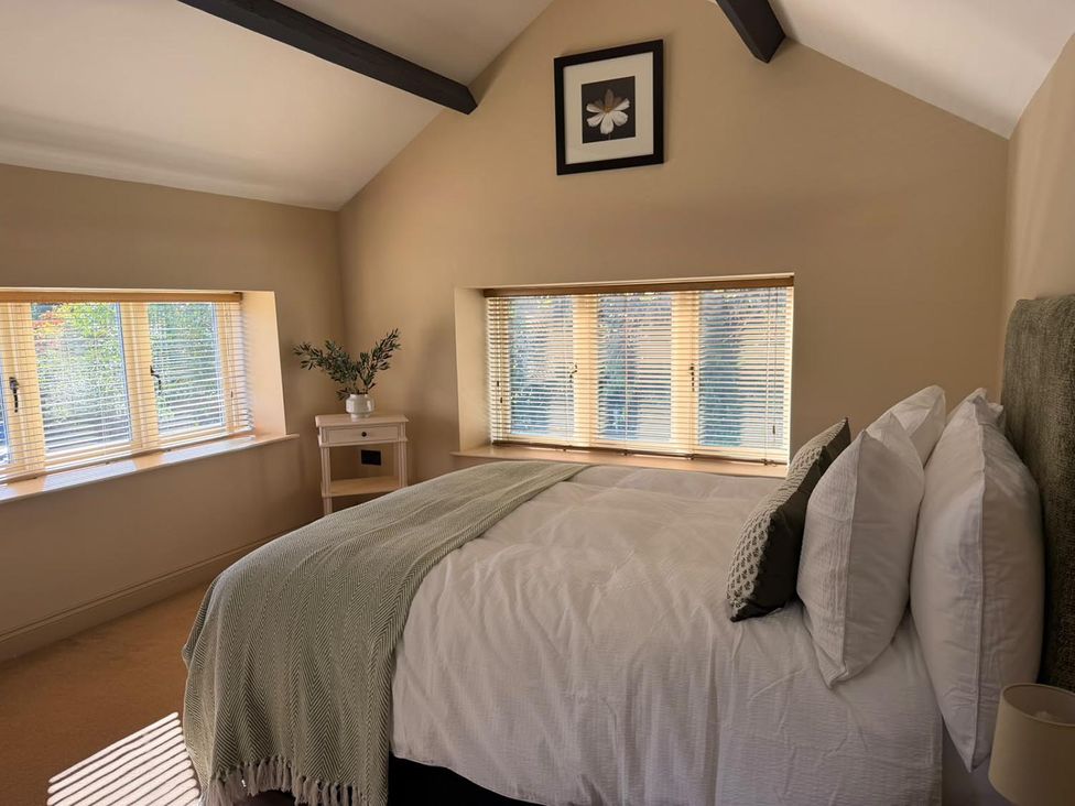 A bedroom with a bed and windows at Honey Pot Cottage near Harrogate