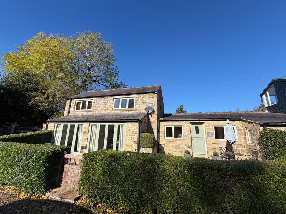An outdoor view of a house with a hedge and patio furniture at Honey Pot Cottage near Harrogate