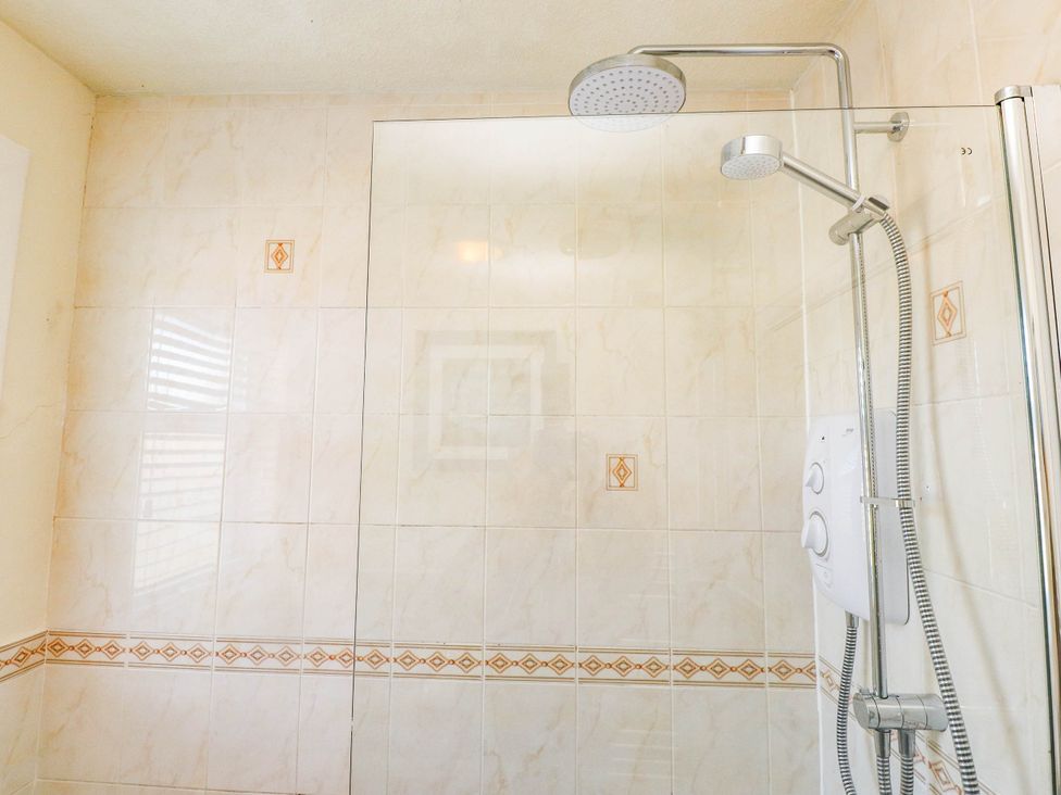 A shower with a glass partition and a shower head at Carol Ann Llandudno